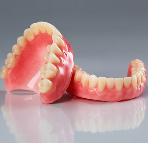 Two pink dental dentures displayed on gray surface showing artificial teeth construction.