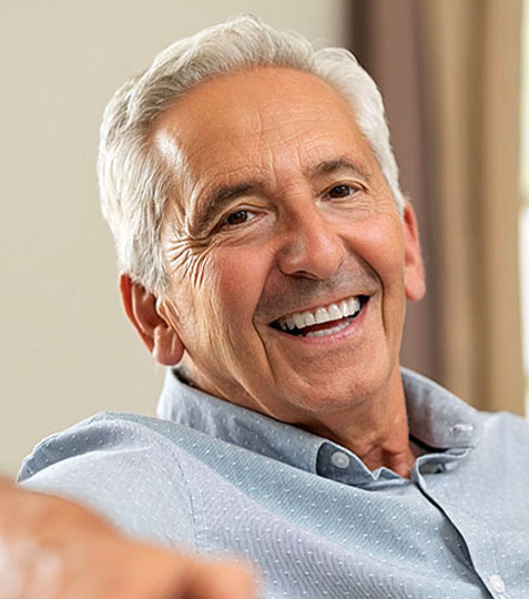 Smiling senior man in light blue shirt, indoor setting with neutral background.