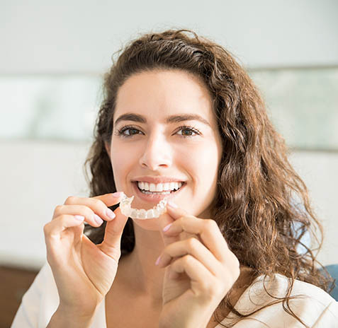 Woman smiling while holding dental floss in bright, clean dental office setting.